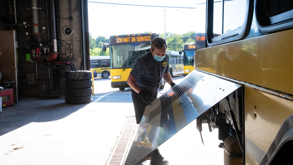 student mechanic opens a side panel of a bus