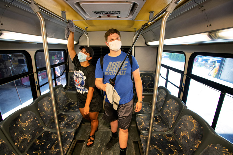 Women left and man right inside bus cleaning and wearing face masks