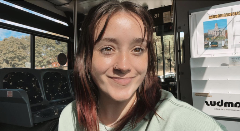 person sitting on bus wearing pale green shirt with close mouth smile