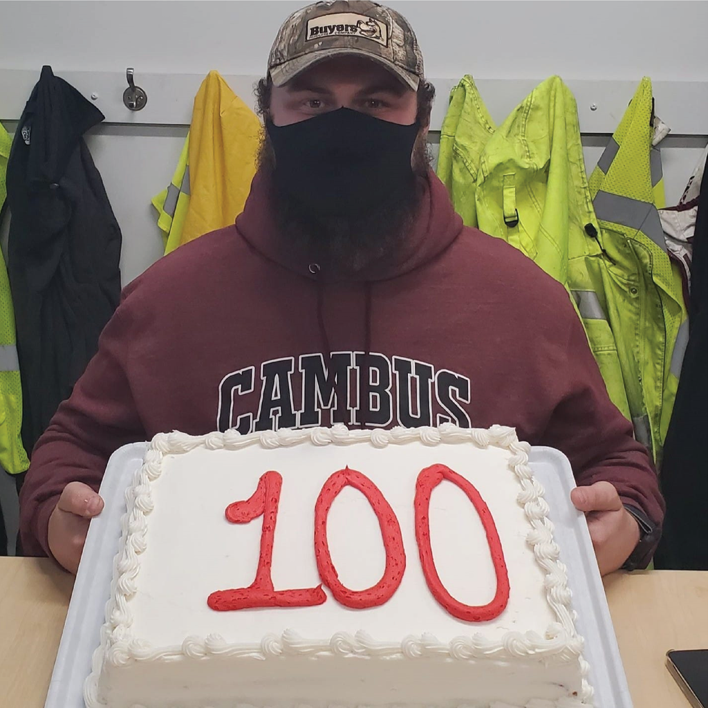 Jason sits at a table with a cake with the number 100 on it