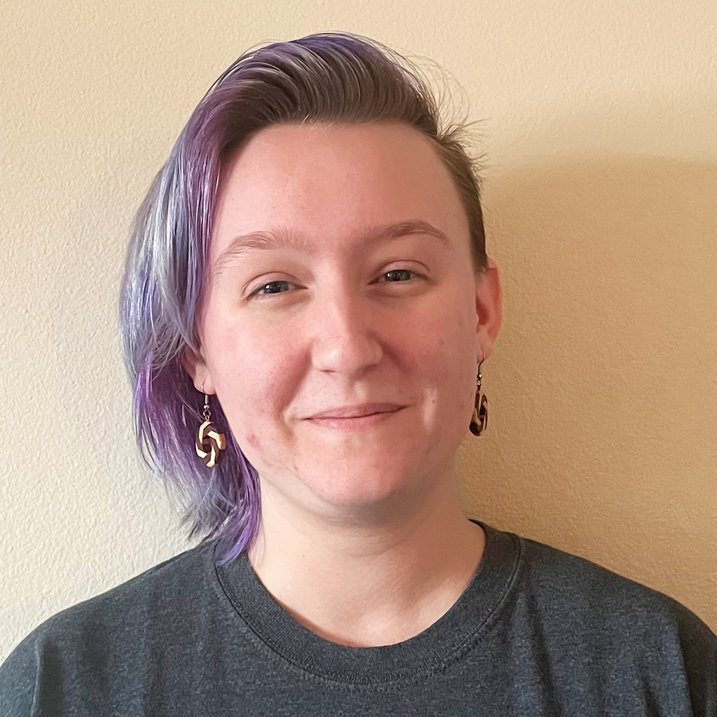 person wearing dark grey shirt smiling with chin length blonde and purple hair