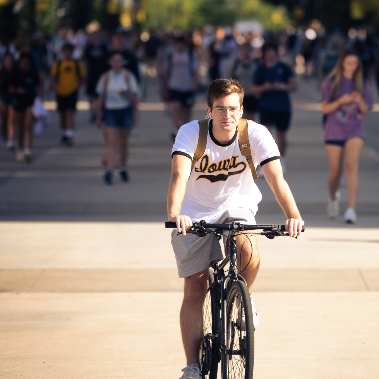 A biker wearing an "Iowa" shirt riding past other students on T. Anne Cleary walkway