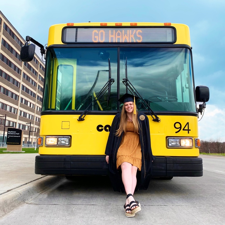 CAMBUS student standing in front of a CAMBUS, wearing a graduation cap and gown