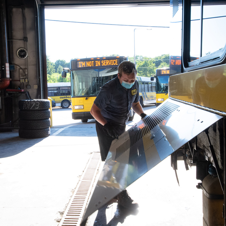 student mechanic opens a side panel of a bus