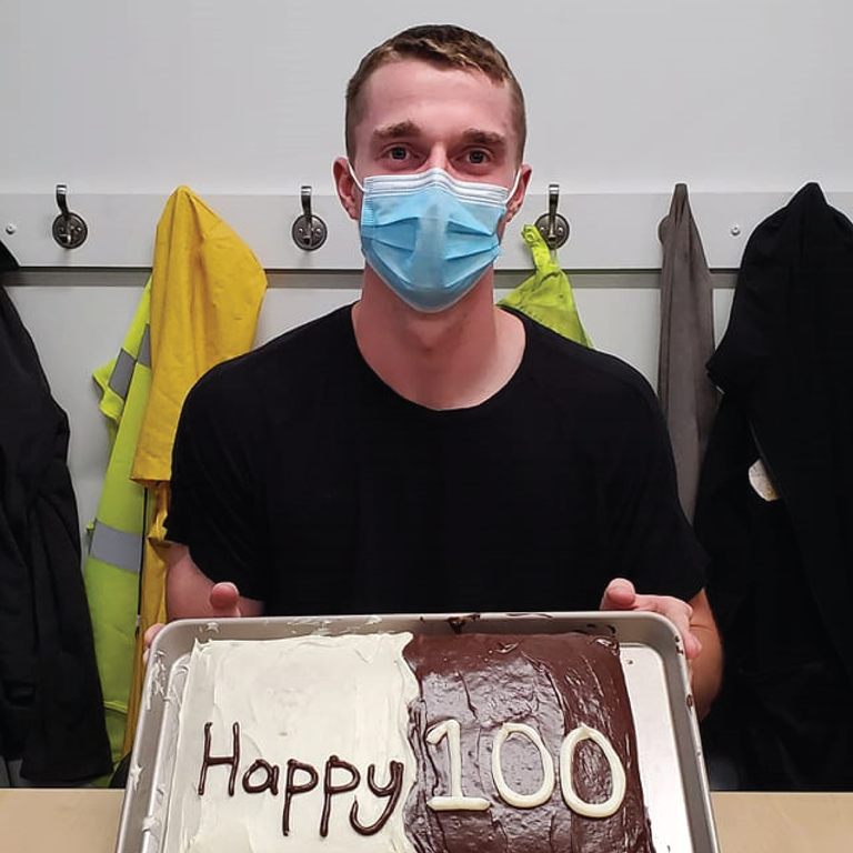 Ethan sits at a table with a cake that reads "Happy 100"