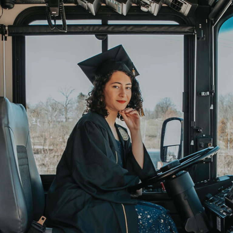 Aurora poses in a cap and gown in the drivers seat of a bus