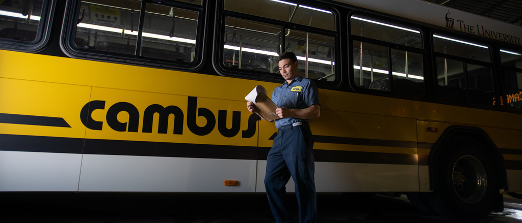 cambus student mechanic looks at clipboard next to a bus