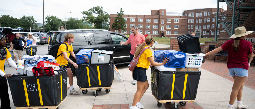 students push carts with belongings towards a residence hall