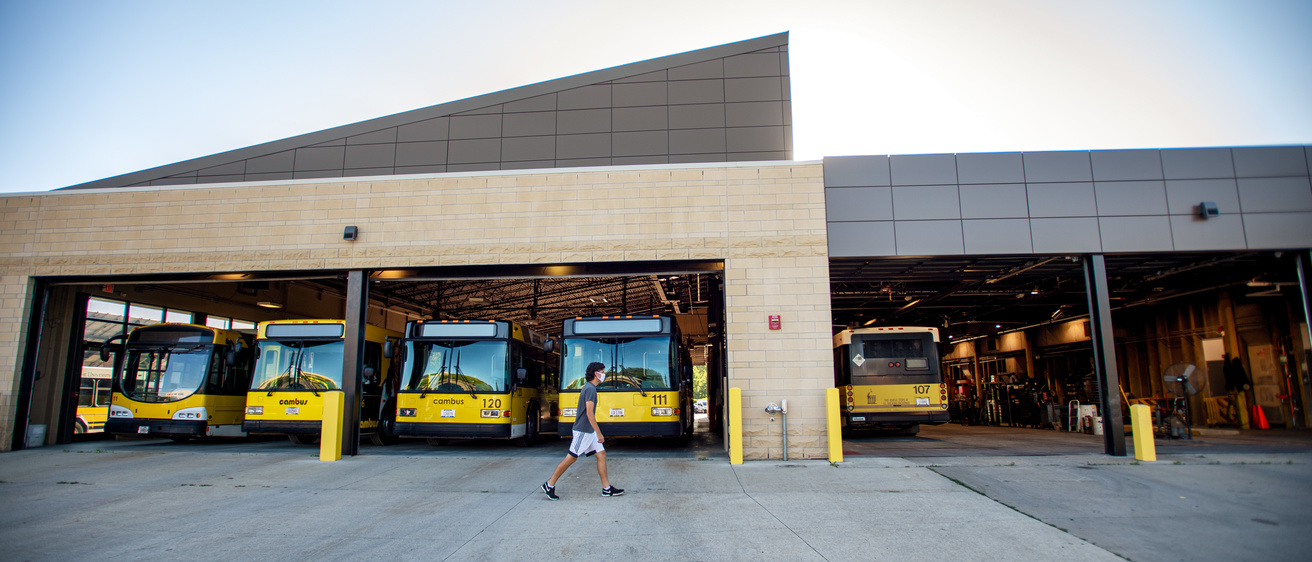 Buses parked in Cambus Maintenance Facility garage with garage doors open and sun shinning brightly behind building