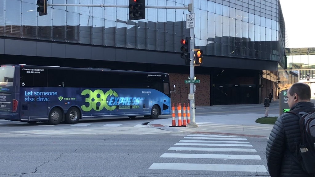 Dark blue bus with green lettering 380Express turns at intersection by stadium with glass facade 