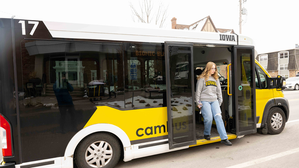 Natalie Kehrli, a Bionic Bus service user, poses aboard Bionic. She has long platinum hair and is wearing red lipstick with black eyeglasses and an "Iowa" sweatshirt.  