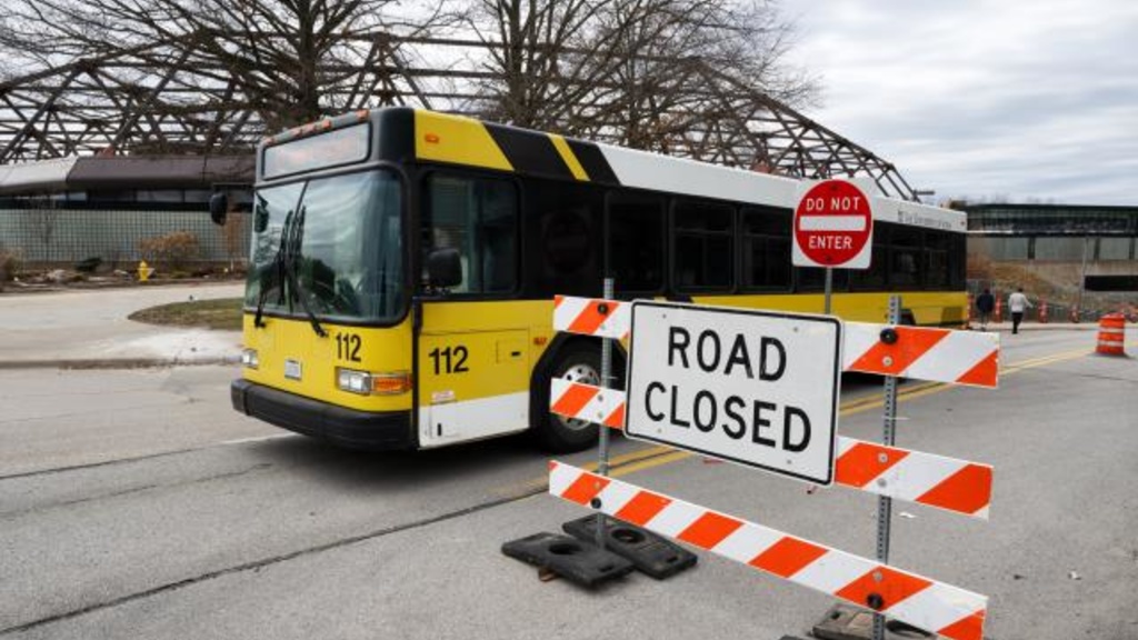 black and gold bus driving near orange and white road closed sign