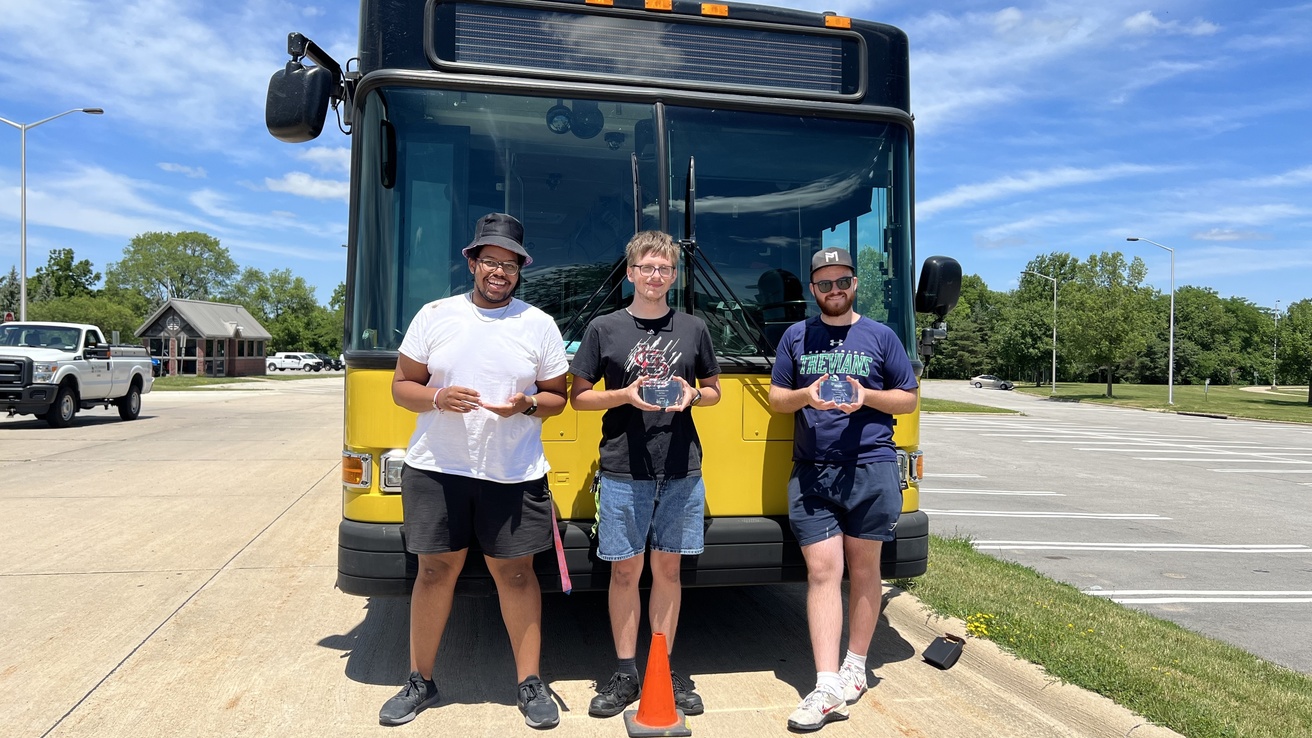 Three CAMBUS drivers pose in front of a CAMBUS holding awards