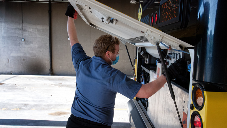 cambus student mechanic opens engine compartment of bus